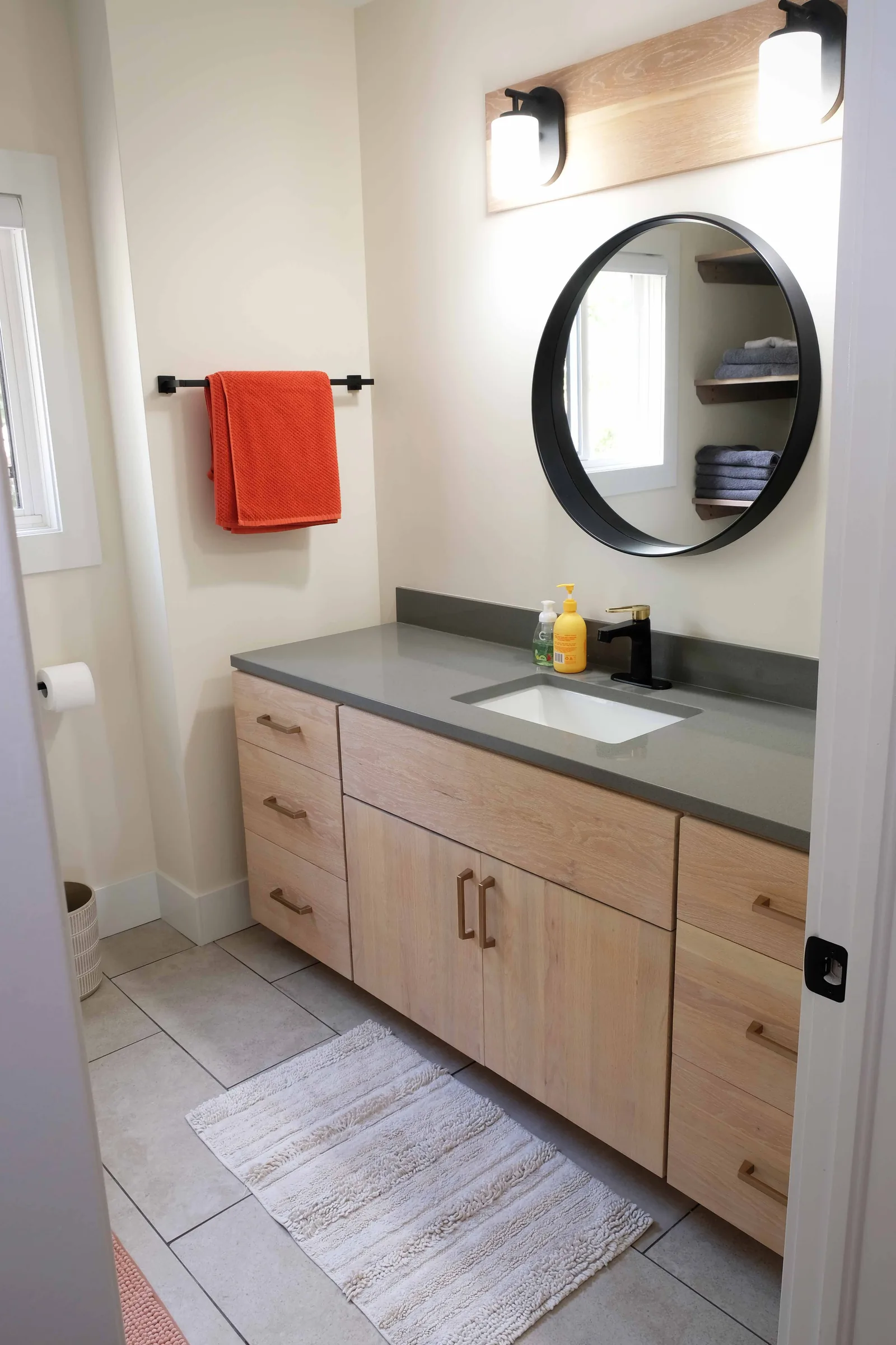 Bathroom vanity in light wood with a round mirror above