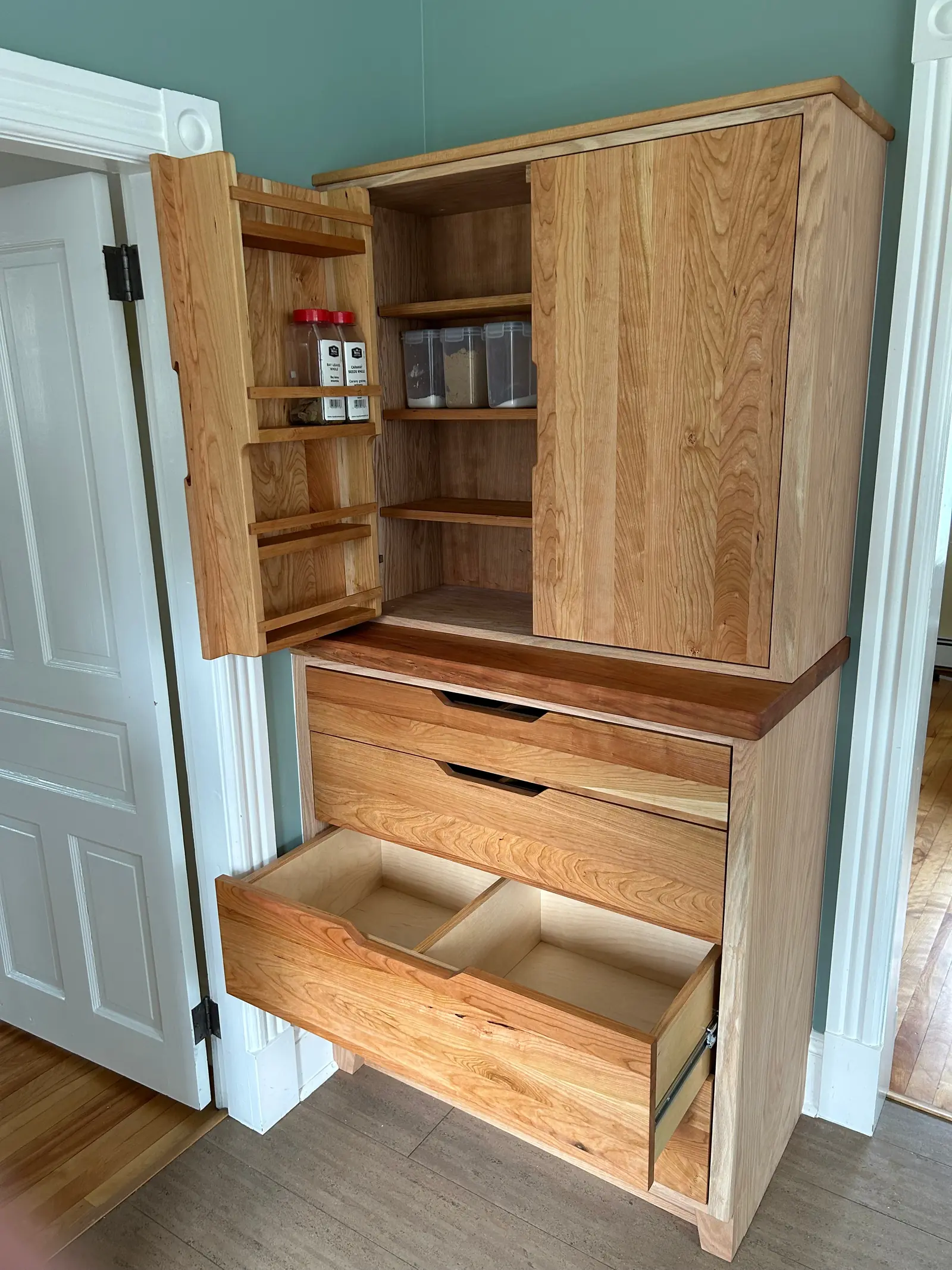 Built-in pantry with open doors showing spice racks, shelves and drawers