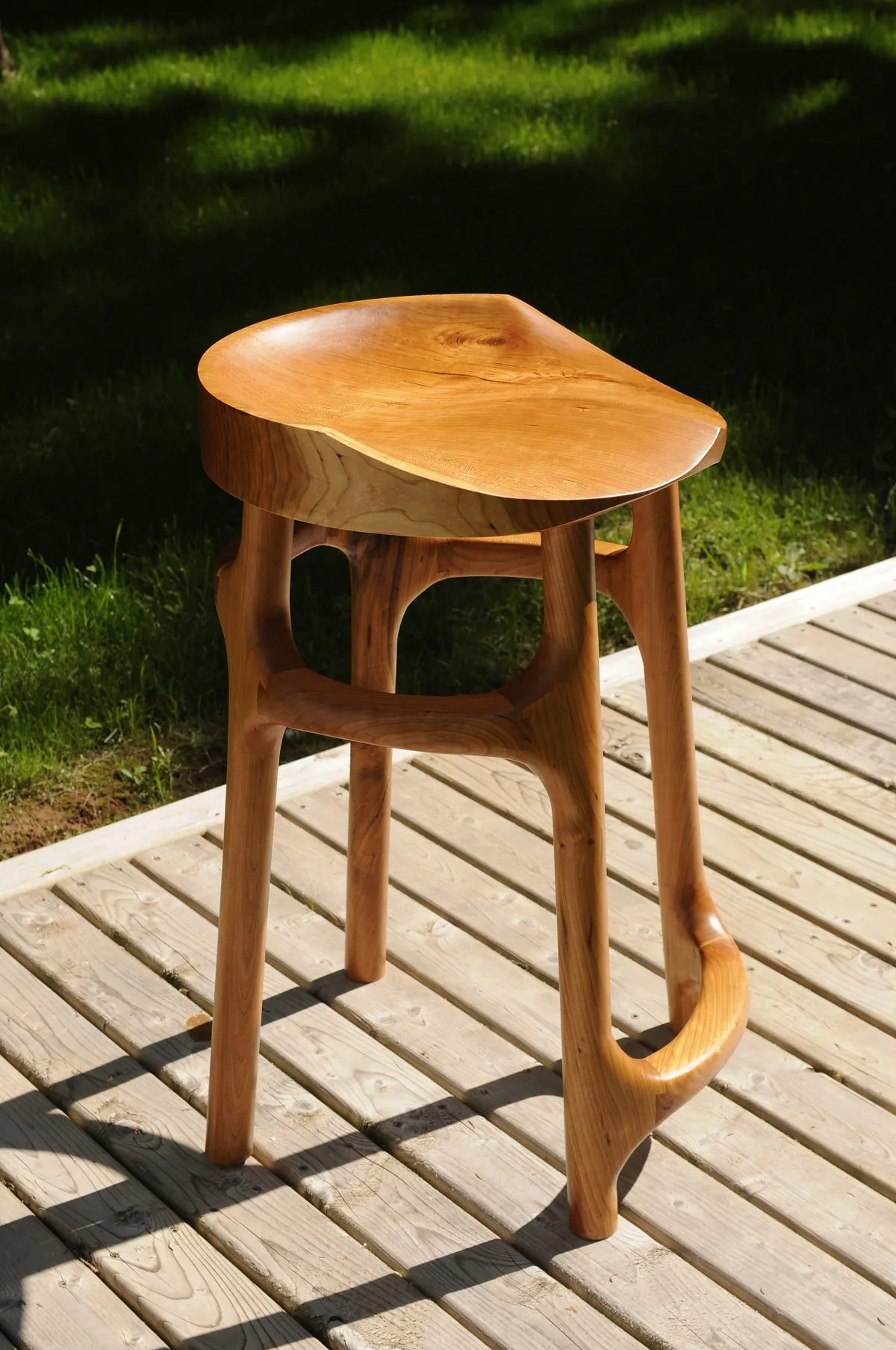 Carved cherry stool with curved legs on a deck