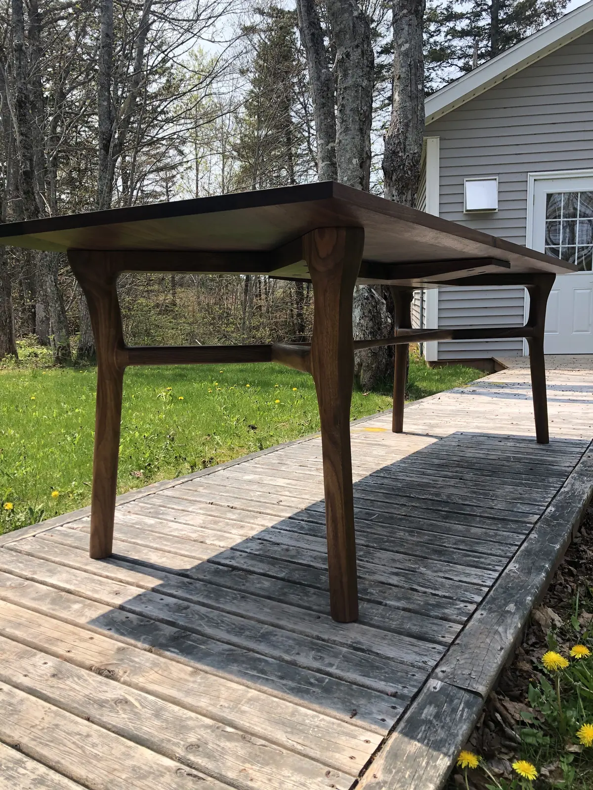 Walnut dining table on a deck, seen from low down to show its legs