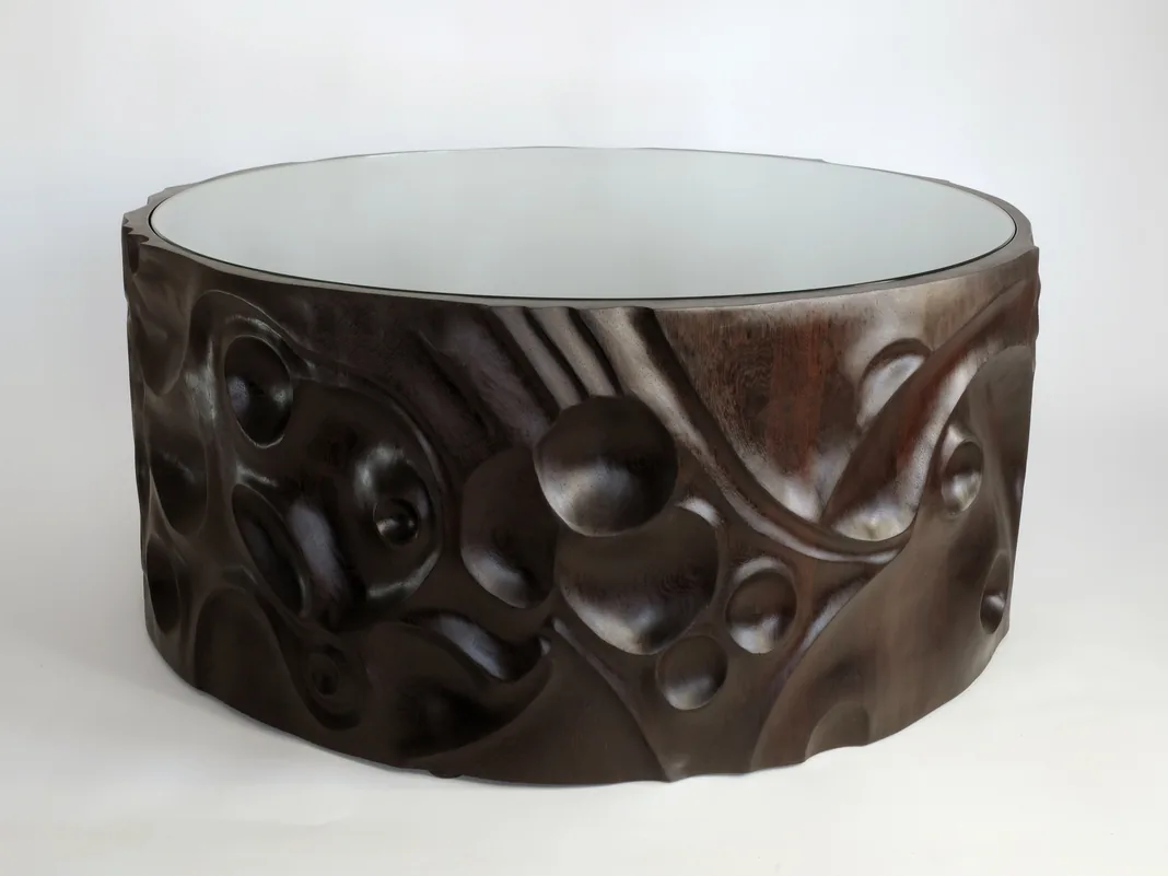 Round wenge coffee table with a carved, sculpted outer wall and an inset glass top